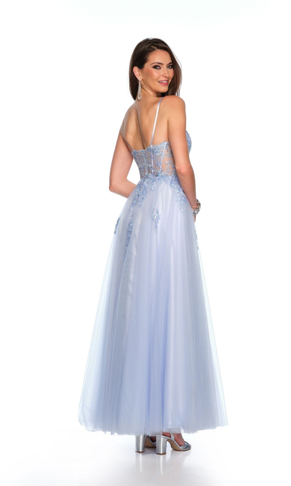 Woman in the Long Formal Dress 11614 by Dave and Johnny—a pastel sky blue gown with lace details, thin straps, and a sheer sweetheart bodice—smiling over her shoulder against a white background.